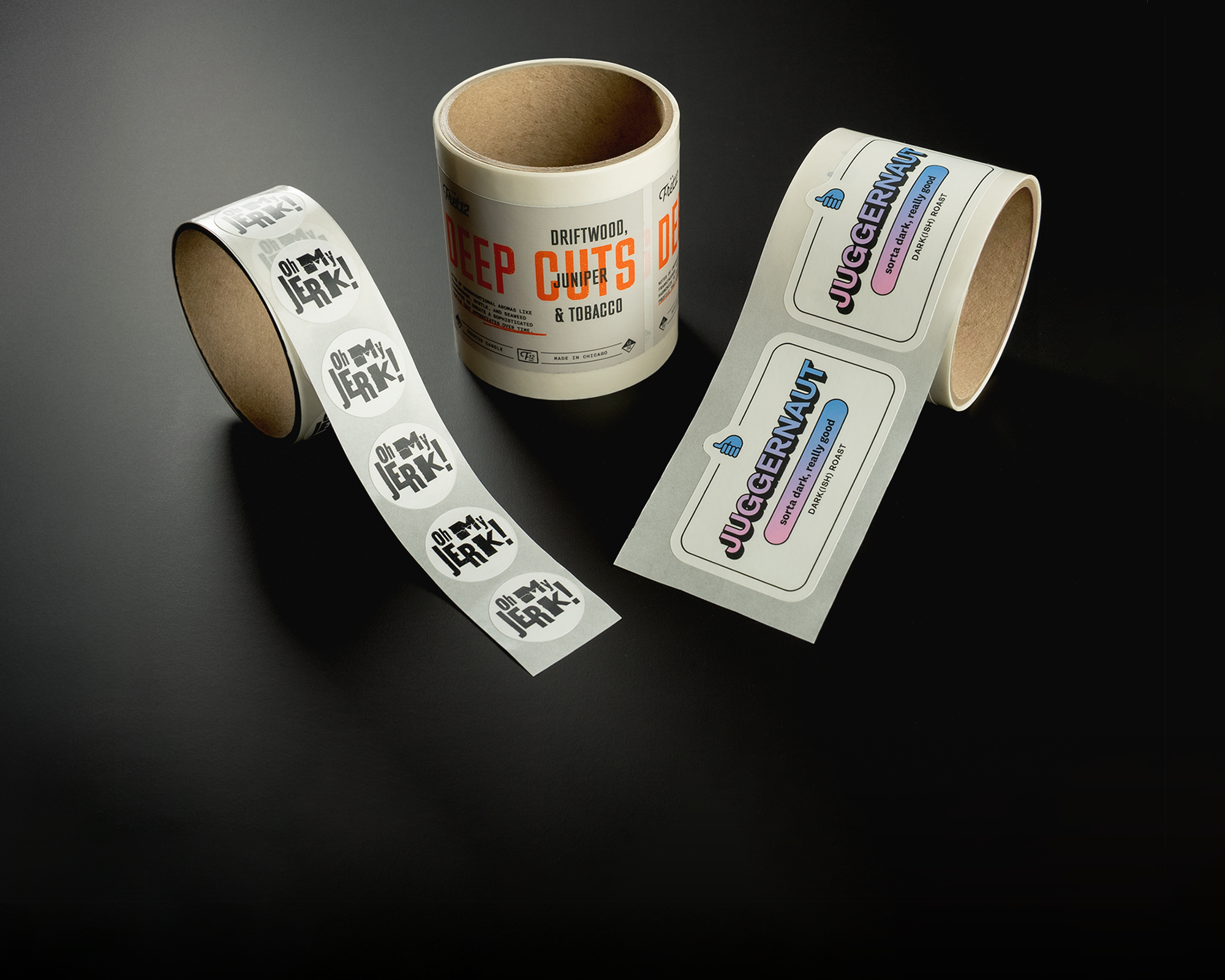 Three rolls of printed labels on a dark surface, featuring "Deep Cuts" and "Juggernaut" designs in various colors and fonts.